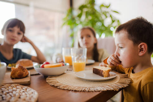 Three siblings eating breakfast in the morning, before school. Back to school, eating homemade breakfast. Importance of eating breakfast before school. - HPIF32177