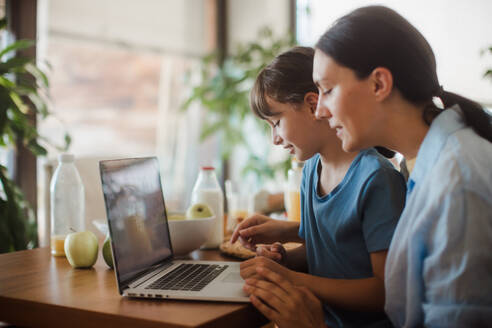 Mutter und Tochter sehen sich unterhaltsame Videos auf dem Arbeitslaptop der Mutter an. Fernarbeit und Heimbüro für alleinerziehende Mutter mit Kindern. - HPIF32190
