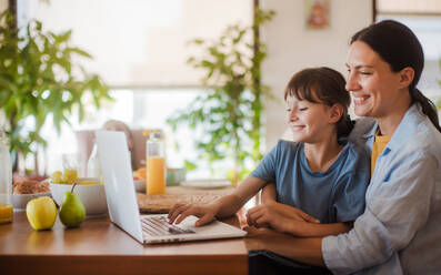 Mutter und Tochter sehen sich unterhaltsame Videos auf dem Arbeitslaptop der Mutter an. Fernarbeit und Heimbüro für alleinerziehende Mutter mit Kindern. - HPIF32191