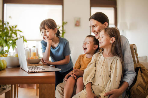 Mutter und Kinder sehen sich unterhaltsame Videos auf dem Arbeitslaptop der Mutter an. Fernarbeit und Heimbüro für alleinerziehende Mutter mit Kindern. - HPIF32192