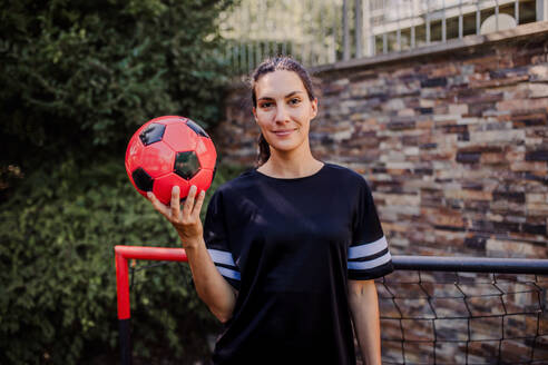 Beautiful female football player standing by the football goal with a ball in her hand. The woman plays soccer for relaxation. Concept of mental health and sport. - HPIF32196