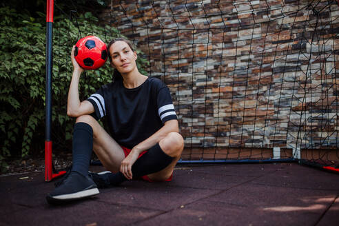 Beautiful female football player standing by the football goal with a ball in her hand. The woman plays soccer for relaxation. Concept of mental health and sport. - HPIF32197