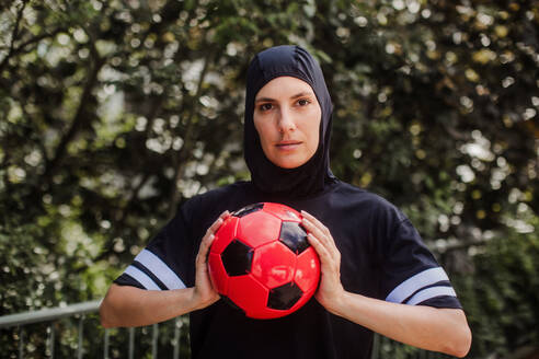 Beautiful female football player in hijab with a ball in her hand. The woman plays soccer for relaxation. Concept of muslim woman in sport. - HPIF32202