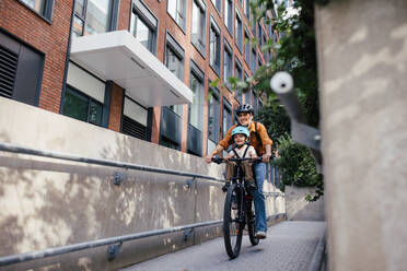 Mutter, die ihren Sohn auf einem sicheren Kinderfahrradträger oder -sitz trägt, beide mit Helm. Mutter, die mit einem kleinen Kind auf dem Fahrrad durch die Stadt fährt. - HPIF32207