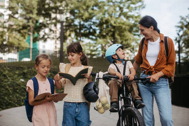 Die Mutter holt ihre Töchter von der Schule ab, der kleine Sohn sitzt auf dem Fahrrad. Die Schülerinnen erzählen ihrer Mutter von ihrem Schultag und gehen vor dem Schulgebäude spazieren. - HPIF32213