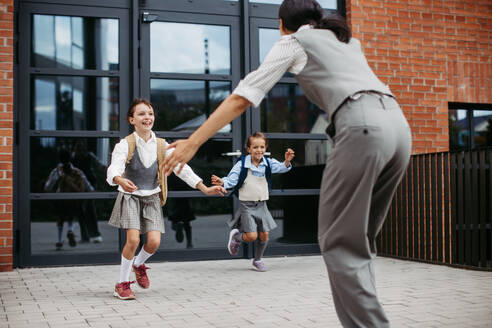 A hard-working, ambitious mother picking up daughters from school, greeting them in front of the school building, and heads to work. Concept of work-life balance for women. - HPIF32216