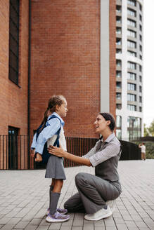 Eine berufstätige Mutter verabschiedet sich vor dem Schulgebäude von ihrer Tochter und macht sich auf den Weg zur Arbeit. Konzept der Vereinbarkeit von Beruf und Familie für Frauen. - HPIF32221