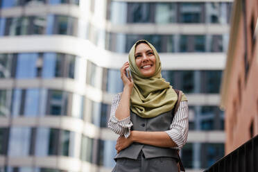 Beautiful woman in hijab making a phone call on a city street. Muslim businesswoman has a business call outside in the city, heading to a meeting. - HPIF32231