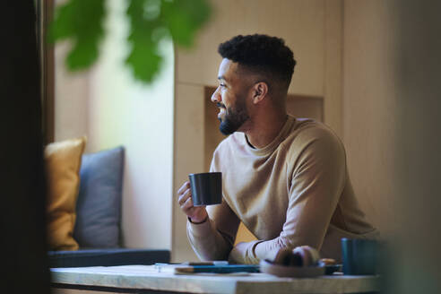 A happy young man with coffee sitting indoors in a tree house, weekend away and individual traveling concept. - HPIF32233