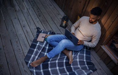 A happy young man with laptop resting outdoors in a tree house, weekend away and remote office concept. Working late at night. High angle shot. - HPIF32237