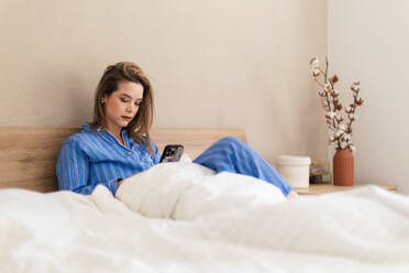 Junge Frau liegt auf ihrem Bett und scrollt auf ihrem Smartphone. - HPIF32239