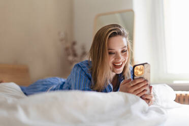 Junge Frau liegt auf ihrem Bett und scrollt auf ihrem Smartphone. - HPIF32241