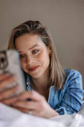 Junge Frau liegt auf ihrem Bett und scrollt auf ihrem Smartphone. - HPIF32242