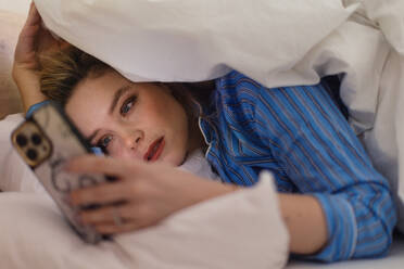 Junge Frau liegt auf ihrem Bett und scrollt auf ihrem Smartphone. - HPIF32247