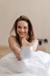 Happy woman sitting on her bed with a cup of coffee. - HPIF32250