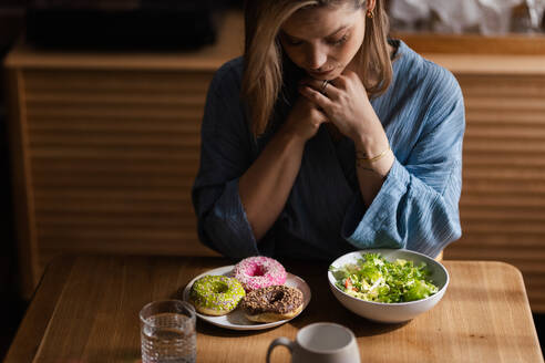 Young woman having diet, deciding between a salad and donuts. - HPIF32253