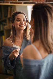 Young woman doing her make-up, looking in a mirror. - HPIF32254