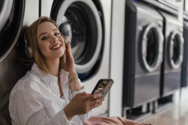 Junge Frau hört Musik und sitzt in einer Waschküche. - HPIF32261
