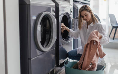 Young woman loading washing machine in a public laundry. - HPIF32262