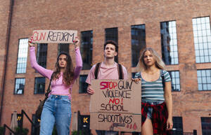 Generation Z activists with banners protesting on the street. Young zoomers students marching through the city demonstrate against climate change. Protesters demanding gun control, racial and gender equity. Concept of power of friendship and social strength of gen Z. - HPIF32290