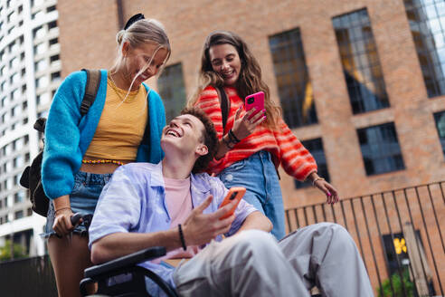 Handsome gen Z boy in a wheelchair with friends in the city. Inclusion, equality, and diversity among Generation Z. - HPIF32303