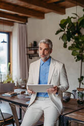 Portrait of handsome businessman leaning against a desk in a modern office. Male corporate leader, executive, manager using digital tablet. - HPIF32319