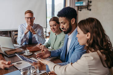 Young colleagues having casual discussion during meeting in office. Group of men and women sitting in conference room. - HPIF32324