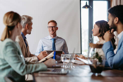 Young colleagues having casual discussion during business meeting in office. Group of men and women sitting in conference room. - HPIF32325