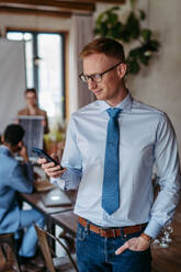 Portrait of confident young businessman using smart phone during meeting. Group of men and women sitting in conference room. - HPIF32340