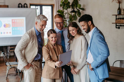 Young colleagues having meeting in an office. Portrait of successful creative business team standing together and looking at tablet. - HPIF32351