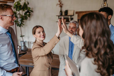 Happy successful multiracial business team giving a high fives gesture as they laugh and cheer their success - HPIF32353