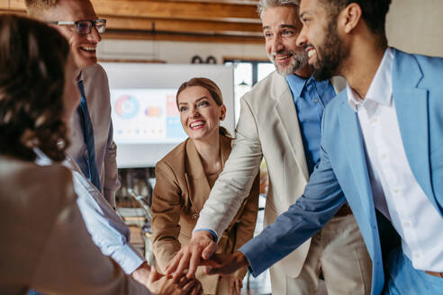 Happy business team stacking hands together to cheer up as they laugh and celebrating their success. Diversity in team work. - HPIF32354