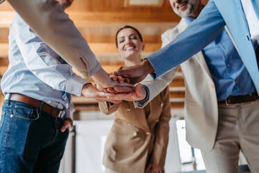 Close up of young colleagues holding hands together, symbol of success and cooperation. - HPIF32355