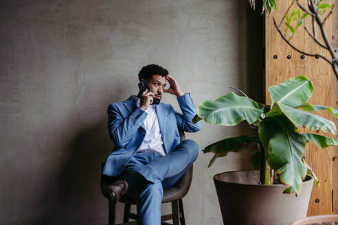 Portrait of a young businessman sitting near window in green office full of plants. - HPIF32369