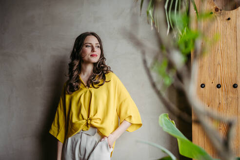 Portrait of a young woman standying near window in green office full of plants. - HPIF32378