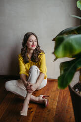 Portrait of a young woman sitting near window in room full of plants. Full length portrait of beautiful caucasian female entrepreneur. - HPIF32379