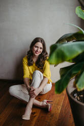 Portrait of a young woman sitting near window in green office full of plants. - HPIF32380