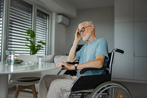 Porträt eines älteren Mannes im Rollstuhl, der zu Hause Tabletten einnimmt, er ist verwirrt über die Verwendung der Medikamente. Chronisch kranker Mann hat kein Geld für seine Medikamente. - HPIF32400