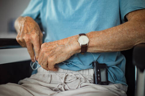 Senior man checking his blood sugar level on an insulin pump. Close up of senior man in wheelchair with type 1 diabetes. - HPIF32402