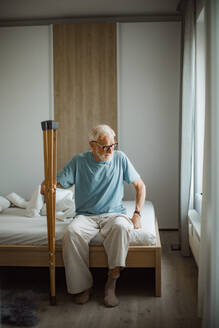 Porträt eines älteren Mannes mit Krücken, der versucht, aus dem Bett aufzustehen. - HPIF32404