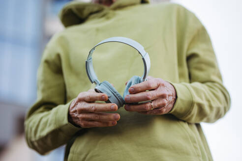 Close up of elderly man holding wireless headphones, listening to music while exercising outdoors. - HPIF32412