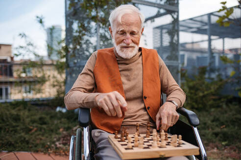 Älterer Mann, der allein im Freien Schach spielt, Klient eines Pflegeheims, der sich an einer Partie Solitärschach erfreut, Schachpuzzle. - HPIF32419