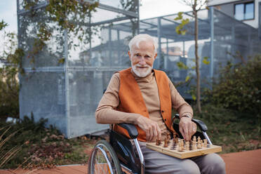 Älterer Mann, der allein im Freien Schach spielt, Klient eines Pflegeheims, der sich an einer Partie Solitärschach erfreut, Schachpuzzle. - HPIF32420