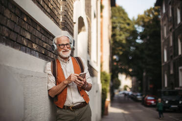 Close up shot of a senior man on the street. Elderly cool man listening to music outdoors, having fun. Concept of old man young at heart. - HPIF32429