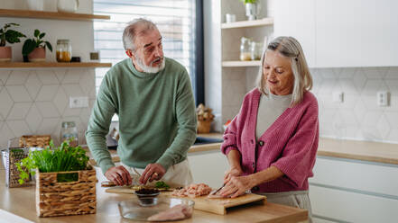 Senior couple cooking together in the kitchen, preparing chicken for dinner. Spending quality time together. - HPIF32460