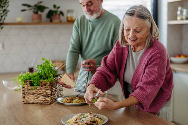 Senior couple cooking together in the kitchen, preparing pasta for dinner. Spending quality time together. - HPIF32479