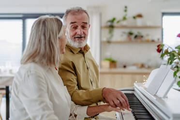 A senior couple sitting side by side at the piano, playing together. - HPIF32488