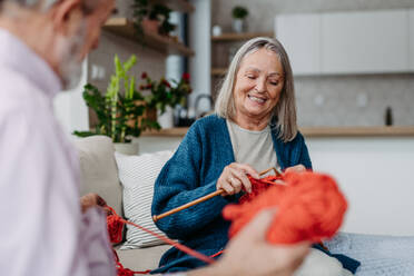 Senior couple knitting together in the living room. - HPIF32498