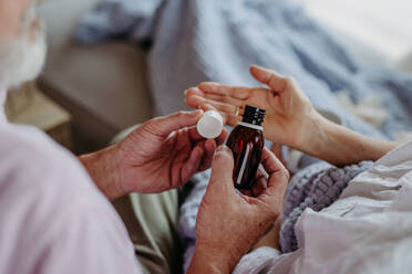 Close up of senior man giving pills to his ill wife. Taking prescribed medication. - HPIF32510