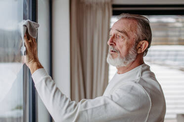 Senior man cleaning windows in his apartment.. - HPIF32512